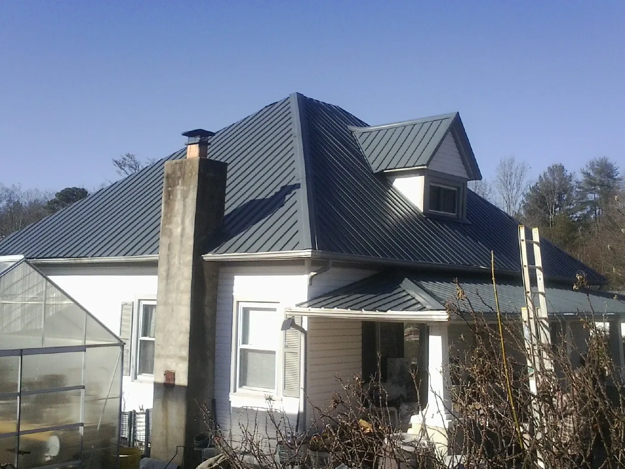 Dark blue standing seam metal roof on a white farmhouse with dormer — Slate & Tile Roof Repair by Roofing Brothers in Big Sandy