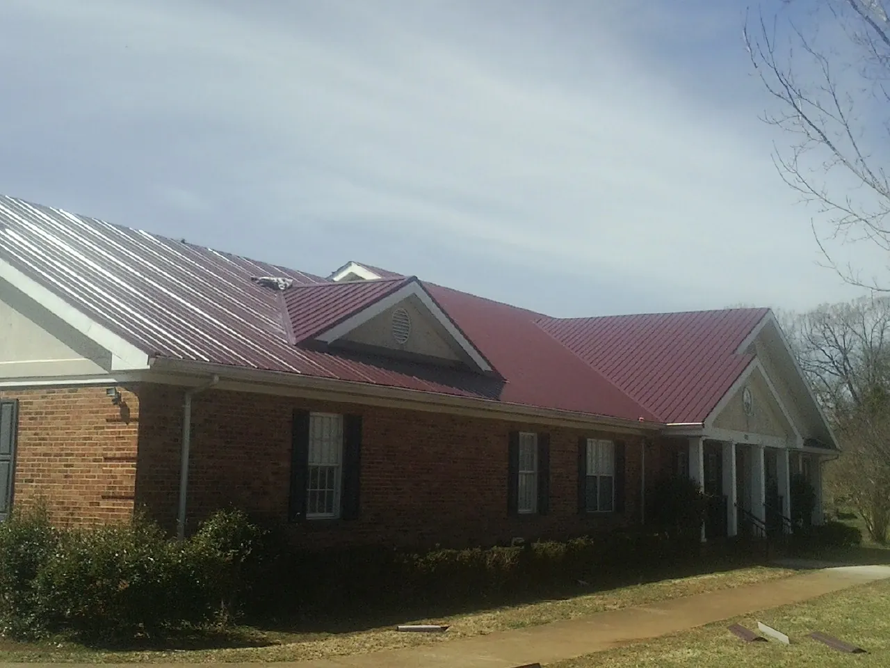 Red metal roof with gabled entries on a long brick building, from a Hail Damage Roof Repair job in Big Sandy
