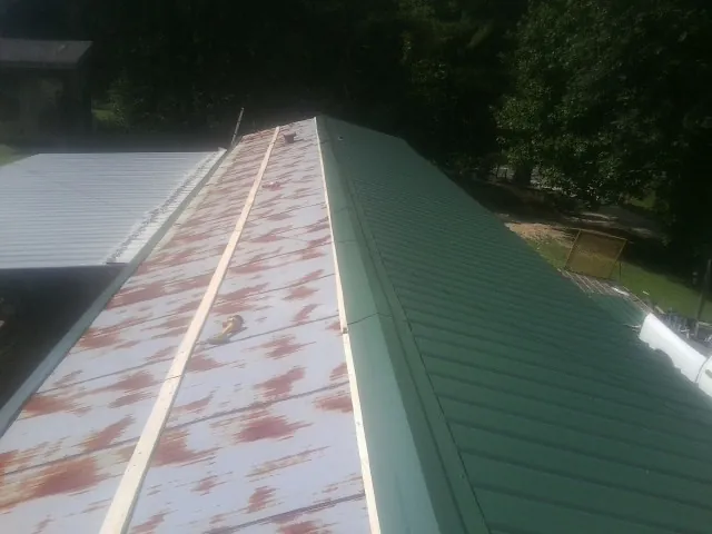 Old rusted panels beside newly installed green metal roofing — Wind Damage Roof Repair by Roofing Brothers in Big Sandy