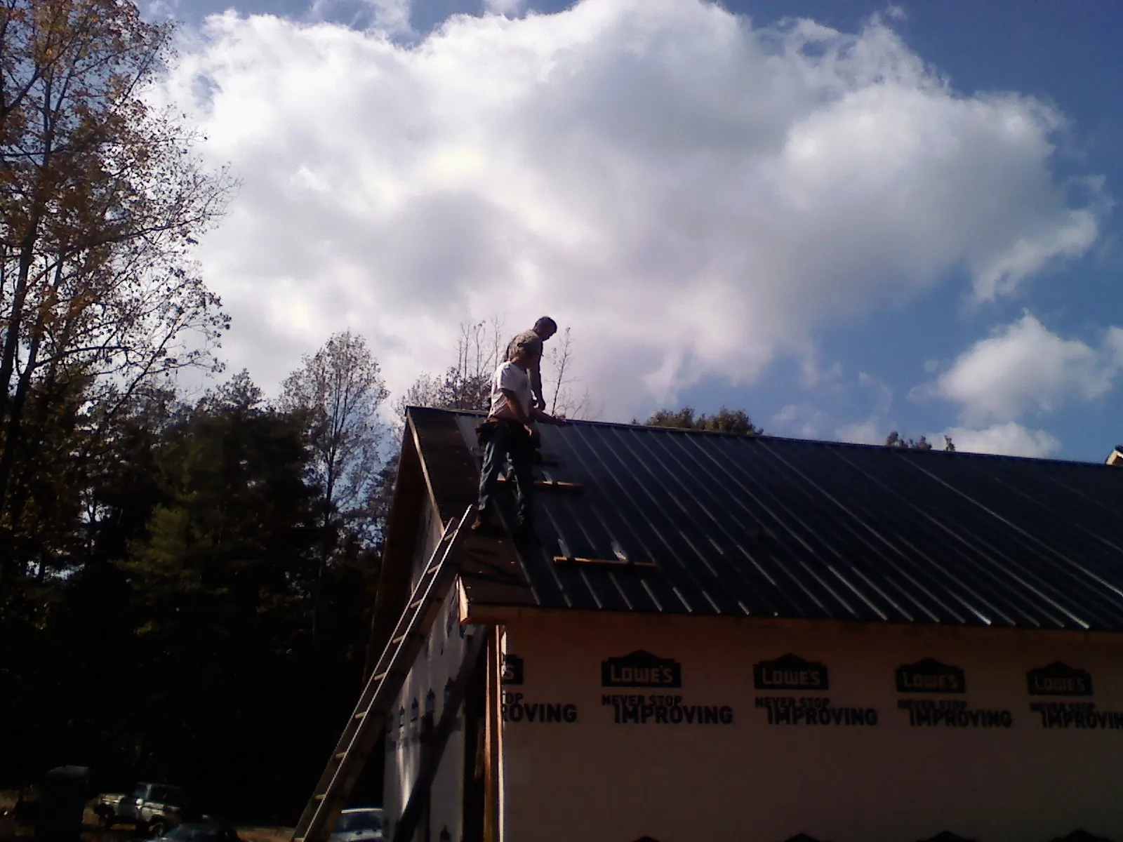 Roofer fastening dark metal panels high against a cloudy sky, from a Roof Inspection job in Big Sandy