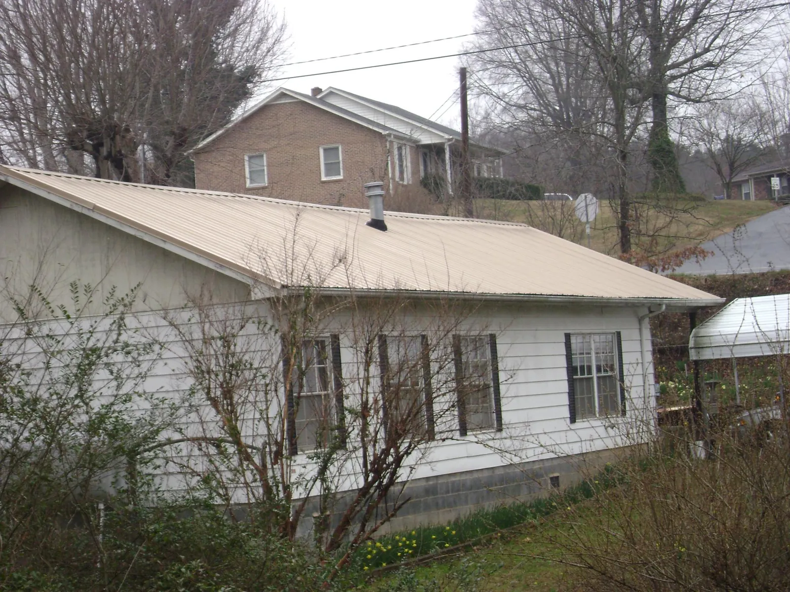 Tan metal roof on a white sided house set into a hillside — Commercial Roofing by Roofing Brothers in Big Sandy