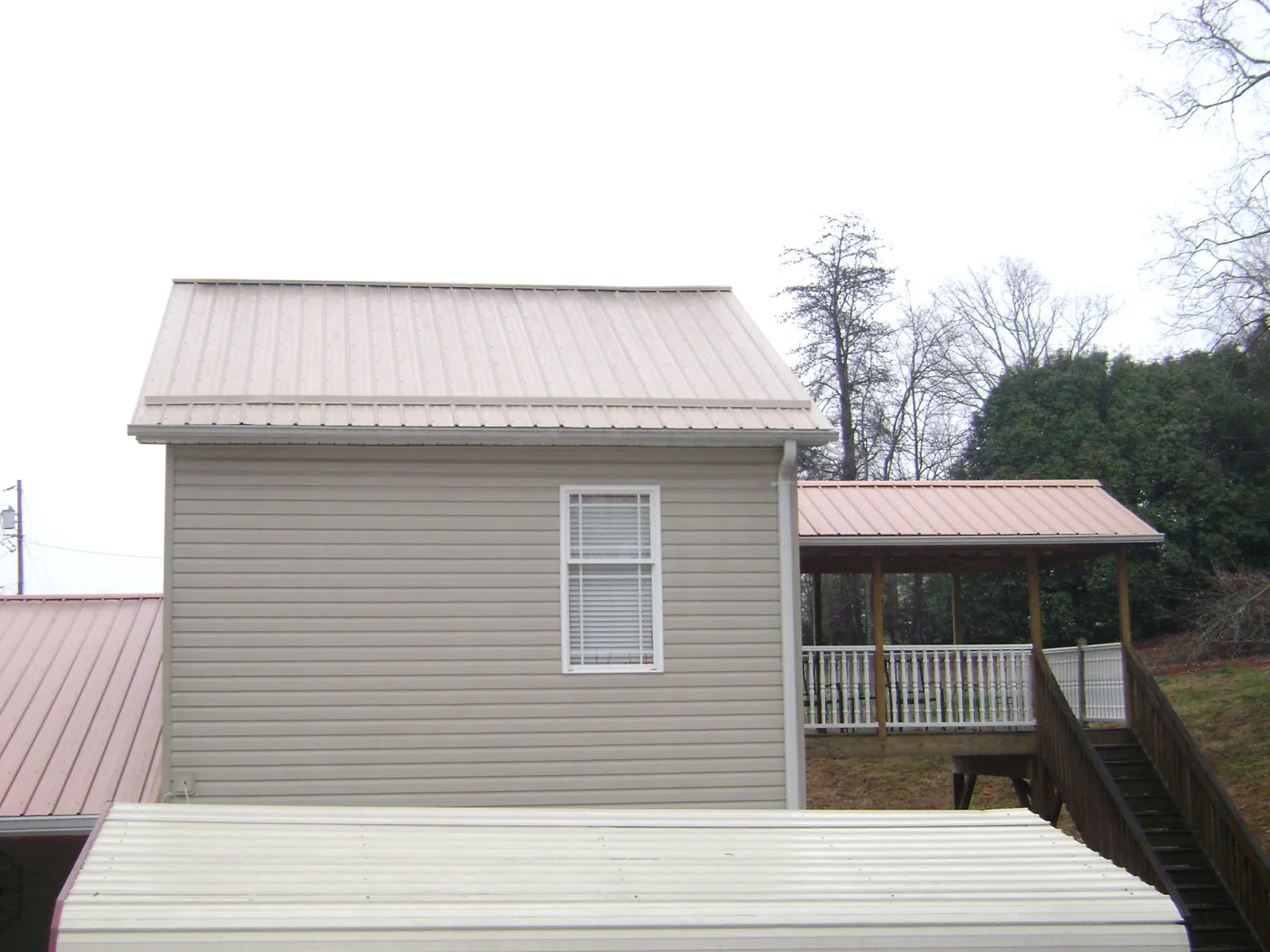 Tan metal roofs on a two story addition and attached porch, from a Roof Replacement job in Big Sandy